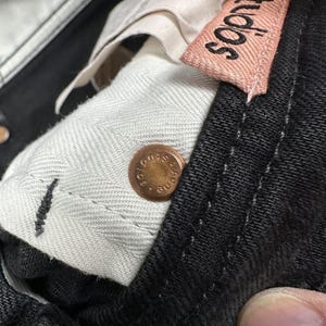 Pode incluir: Cal&ccedil;as de ganga pretas com um rebite de metal cor de cobre gravado com o texto Acne Studios. Uma etiqueta de tecido rosa claro com o texto Acne Studios est&aacute; cosida no c&oacute;s interior, forrado com tecido branco com padr&atilde;o espinha.