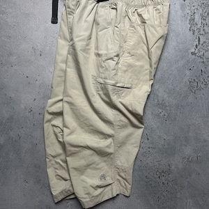 Op de afbeelding: Beige cargo shorts met een zwarte verstelbare riem en een klein driehoekig logo op het linkerbeen.