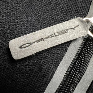 May include: Black zippered pouch with a reflective silver stripe and a gray leather tag with the word "Oakley" printed in white.