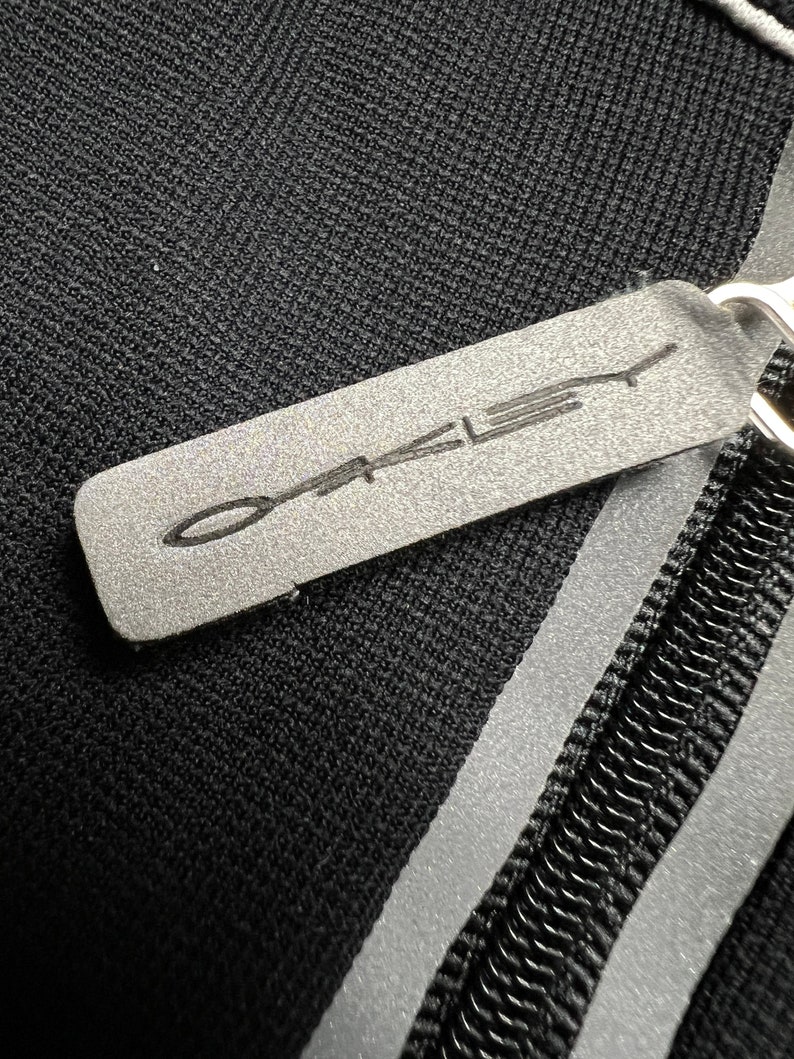 May include: Black zippered pouch with a reflective silver stripe and a gray leather tag with the word "Oakley" printed in white.