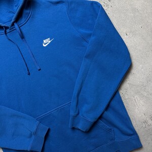 Peut inclure: Un sweat-shirt &agrave; capuche bleu avec un logo Nike blanc sur le devant.
