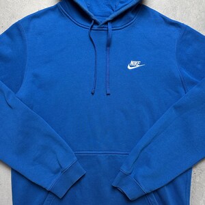 Peut inclure: Un sweat-shirt &agrave; capuche bleu avec un logo Nike blanc sur le devant.