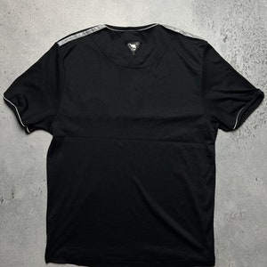 May include: Black t-shirt with a white trim around the neckline and sleeves. The shirt has a small, black triangle logo on the back.