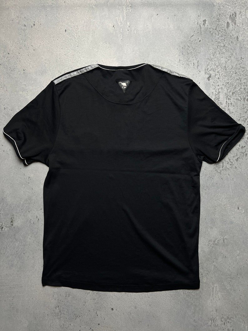 May include: Black t-shirt with a white trim around the neckline and sleeves. The shirt has a small, black triangle logo on the back.
