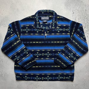 Könnte beinhalten: Ein marineblauer Lands' End Fleece-Pullover mit einem geometrischen Muster in Blau- und Gelbtönen. Der Pullover hat einen Viertel-Reißverschluss und einen Kragen. Das Lands' End-Logo ist auf dem Kragen sichtbar.