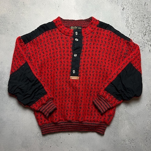 May include: Red and black patterned sweater with a button-up collar and black accents on the sleeves. The sweater has a "Woolrich" label on the front.