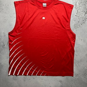 May include: Red sleeveless athletic shirt with a white geometric design on the left side. The shirt has a small logo on the front.