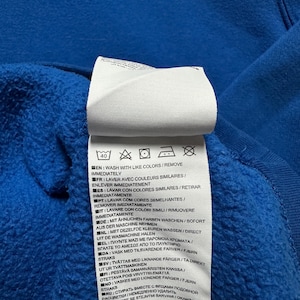 Peut inclure: Une &eacute;tiquette d'entretien blanche avec des instructions de lavage pour un v&ecirc;tement. L'&eacute;tiquette contient du texte dans plusieurs langues, notamment l'anglais, le fran&ccedil;ais, l'espagnol, l'italien, l'allemand, le n&eacute;erlandais, le portugais, le polonais et le su&eacute;dois. L'&eacute;tiquette indique de laver avec des couleurs similaires et de retirer imm&eacute;diatement.