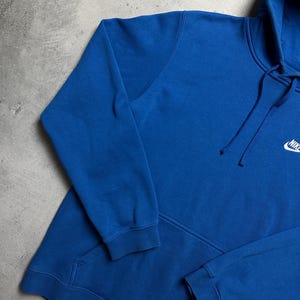 Peut inclure: Un sweat &agrave; capuche bleu royal avec un logo Nike blanc en forme de virgule sur la poitrine gauche.