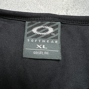 May include: Black Oakley Softwear XL tag with a white Oakley logo and the text "Softwear" and "Oakley, Inc."