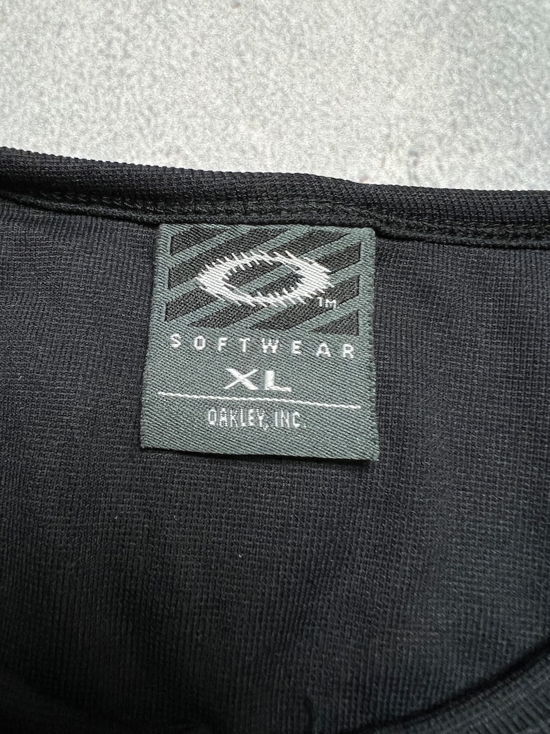 May include: Black Oakley Softwear XL tag with a white Oakley logo and the text "Softwear" and "Oakley, Inc."