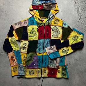 Può includere: Una felpa con cappuccio patchwork colorata con chiusura a zip e cappuccio con coulisse. La felpa è realizzata con diversi tessuti e presenta vari simboli e disegni, tra cui un sole, una foglia e un motivo paisley. La felpa è un capo di abbigliamento vibrante e unico.