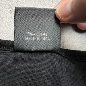 May include: Black fabric tag with white text that reads "RN# 96548 MADE IN USA".
