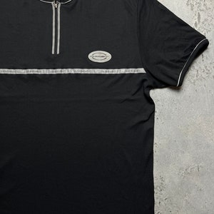 May include: Black short-sleeved t-shirt with a zipper and a silver reflective stripe across the chest. The shirt has a small oval logo with the text "Essential" on it.