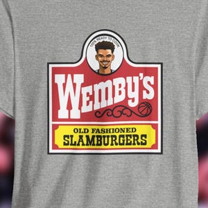 May include: A gray t-shirt with a red and yellow graphic of a basketball player with the text "Wemby's Old Fashioned Slamburgers" and a basketball.