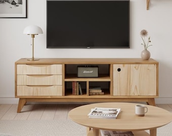 May include: A modern living room featuring a light wood TV stand with drawers and open shelving, a round coffee table, and a white sofa. A framed black and white landscape art piece hangs on the wall.