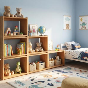 Op de afbeelding: Een modulair houten rek met drie niveaus van open vakken, gevuld met teddyberen, boeken, bouwblokken, een wereldbol en gevlochten opbergmanden. De kast is in een getrapte opstelling geplaatst tegen een lichtblauwe muur in een slaapkamer.