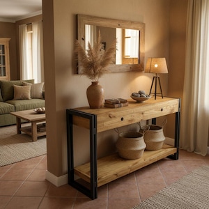 Può includere: Un tavolo console rettangolare con piano e ripiano in legno naturale sostenuti da una struttura in metallo nero. Il tavolo presenta due cassetti con fori circolari, un vaso in terracotta con erba della pampa secca, due libri e una ciotola di pietre.