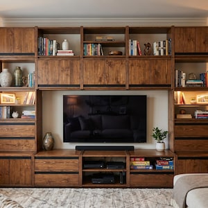 May include: A large, floor-to-ceiling wooden wall unit featuring a dark brown finish with visible wood grain. The unit includes multiple open shelves, closed cabinets, and drawers, surrounding a central television and a black soundbar.