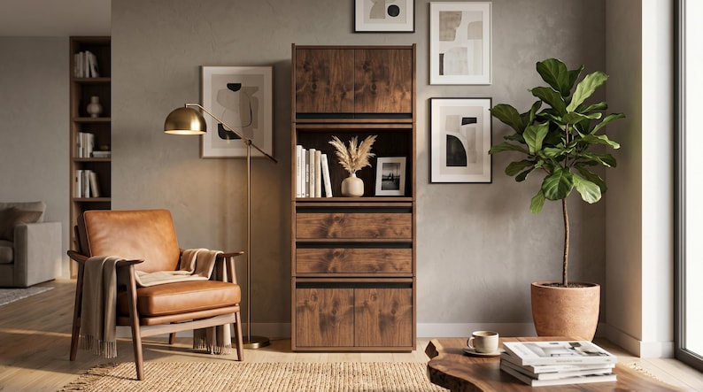 May include: A tall, dark wood storage cabinet featuring two upper doors, two central drawers, and two lower doors. The unit has a visible wood grain pattern and is positioned between a leather armchair and a potted plant in a room setting.