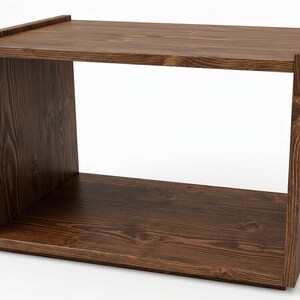 May include: A rectangular open-front storage unit crafted from dark brown wood with a visible grain pattern. The piece features a flat top surface, two solid side panels, and a base, creating a single large open compartment for storage or display.