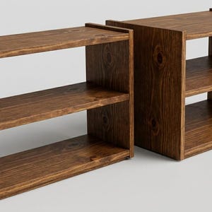May include: Two rectangular wooden shelving units featuring a dark brown finish with visible wood grain and knots. Each unit consists of three horizontal shelves supported by two vertical side panels, providing an open storage structure.