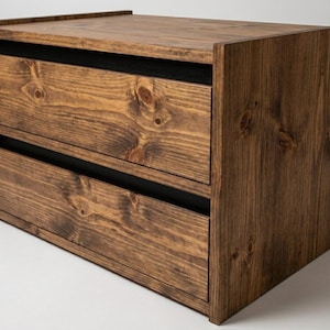 May include: A rectangular wooden storage unit featuring two horizontal drawers with visible wood grain patterns and knots. The unit is constructed from dark brown stained wood with black accents between the drawer fronts and the frame.