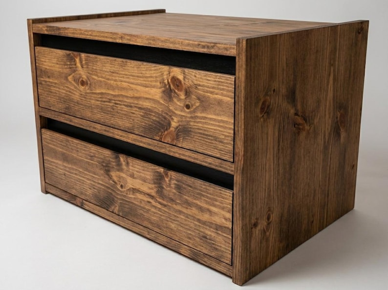 May include: A rectangular wooden storage unit featuring two horizontal drawers with visible wood grain patterns and knots. The unit is constructed from dark brown stained wood with black accents between the drawer fronts and the frame.