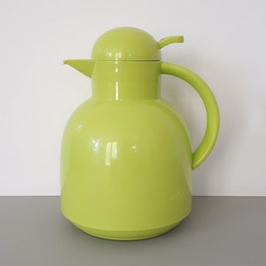 May include: A bright green thermal carafe with a rounded body and a handle. The carafe has a lid with a spout and a small handle.