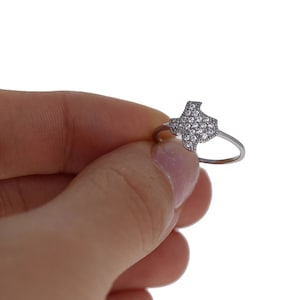 May include: A silver ring with a clear crystal Texas state outline.