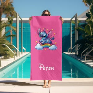 May include: Pink beach towel with a blue Stitch character riding a rainbow. The towel has the name "Peter" printed on it.