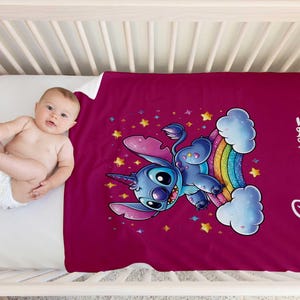 May include: A pink fleece blanket with a blue Stitch character riding a rainbow unicorn. The blanket has a white border and the name "Charlotte" is printed on the right side.