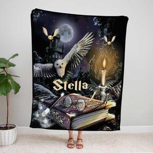 May include: A rectangular fleece blanket featuring a dark fantasy scene with a white owl in flight, a castle, a full moon, a lit candle, round glasses, and a wand resting on a book. The name Stella is printed in large, bold, light-colored letters.