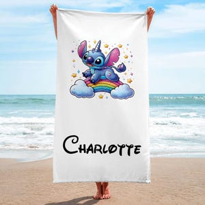 May include: A white beach towel with a blue Stitch character riding a rainbow. The towel has the name "Charlotte" printed on it.