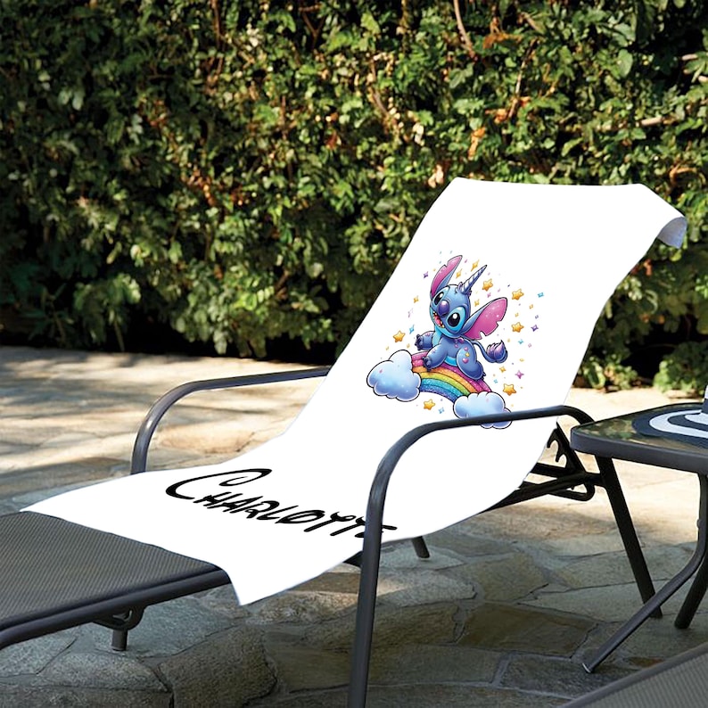 May include: White beach towel with a blue cartoon character riding a rainbow. The character has a unicorn horn and is surrounded by stars. The towel has the name "Charlotte" written on it.