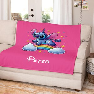 May include: Pink fleece blanket with a blue Stitch character riding a rainbow with stars. The blanket has the name "Peter" printed on it.