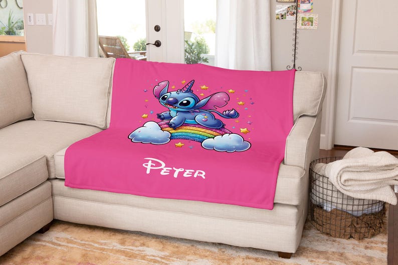 May include: Pink fleece blanket with a blue Stitch character riding a rainbow with stars. The blanket has the name "Peter" printed on it.