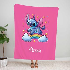 May include: Pink fleece blanket with a blue Stitch character riding a rainbow with a unicorn horn. The blanket has the name "Peter" printed on it.