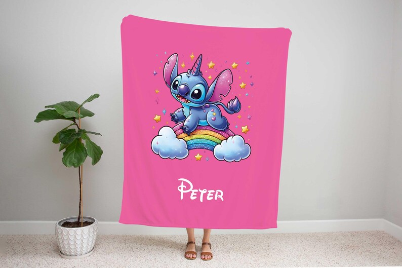 May include: Pink fleece blanket with a blue Stitch character riding a rainbow with a unicorn horn. The blanket has the name "Peter" printed on it.