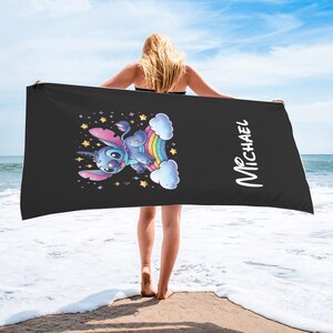 May include: Black beach towel with a blue and purple unicorn character riding a rainbow. The towel has the name "MICHAEL" printed on it.