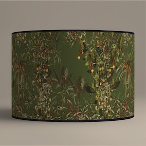 May include: A cylindrical lampshade with a dark green background and a detailed botanical print. The design features various plants, including palm trees, ferns, and flowering vines with red and yellow accents. The lampshade is trimmed with a dark blue border.