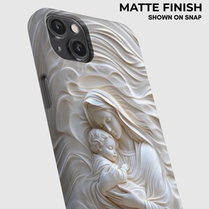 May include: A phone case with a matte finish featuring a raised, cream-colored relief sculpture of a figure holding a child, surrounded by flowing, wave-like patterns. The text MATTE FINISH SHOWN ON SNAP is printed in the upper right corner.