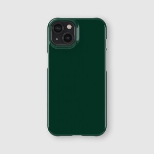 May include: A solid dark forest green smartphone case with a smooth, glossy finish. The case features a rectangular camera cutout in the upper left corner, designed to accommodate a dual-lens camera system and a small circular flash component.