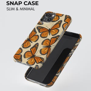 Może przedstawiać: Etui na telefon typu snap case z powtarzającym się wzorem pomarańczowo-czarnych motyli monarch&oacute;w na kremowym tle. Tekst SNAP CASE SLIM & MINIMAL jest wydrukowany na czarno. Etui pokazano od strony zewnętrznej oraz od strony wewnętrznej.