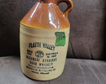 May include: A brown ceramic jug with a label that reads "Platte Valley Since 1856" and "Missouri Straight Corn Whiskey" bottled by McCormick Distilling Co. Weston, Missouri. The label also states "100 Proof 3/4 Pint".