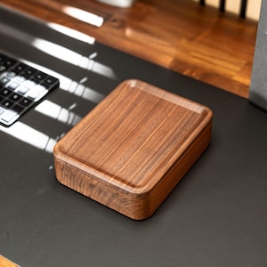 May include: A rectangular wooden box with a lid, crafted from a rich, warm-toned wood. The box sits on a dark surface, with a keyboard visible in the background. The lid has a slightly recessed top, adding a touch of elegance to the design.