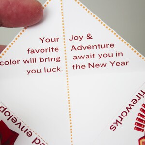 May include: A white paper fortune teller with red text. The text reads "Your favorite color will bring you luck. Joy & Adventure await you in the New Year." The fortune teller has a red and gold design on the outside.