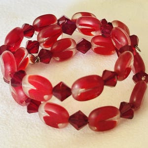 Bracciale avvolgente con perline di vetro rosse, filo a memoria di forma e perline di cristallo color mirtillo rosso.