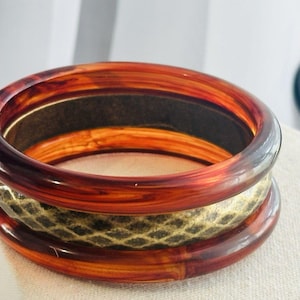 May include: A circular bangle bracelet featuring two smooth, translucent, reddish-brown tortoise shell-patterned outer rings and a central band with a textured, dark green and gold diamond-shaped scale pattern throughout the entire circumference.