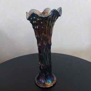 Puede incluir: Un jarrón alto de vidrio azul iridiscente con un diseño texturizado que parece corteza de árbol. El jarrón tiene un borde acampanado y festoneado.